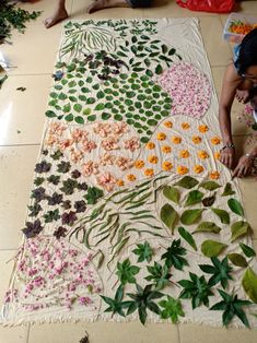 two women are working on an art project with flowers and leaves laid out on the floor