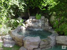 an outdoor pool with waterfall and rocks in the middle, surrounded by greenery on both sides