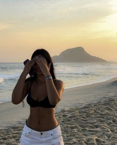 a woman standing on top of a beach next to the ocean holding her hands up to her face