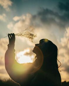 a woman holding her hand up to the sky and blowing seeds in front of her face