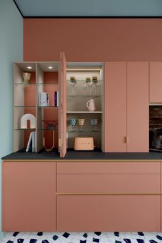 a kitchen with pink cupboards and glass shelves filled with dishes, wine glasses and other items