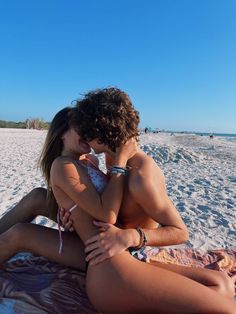 a man and woman are sitting on the beach hugging each other as they look into each others eyes