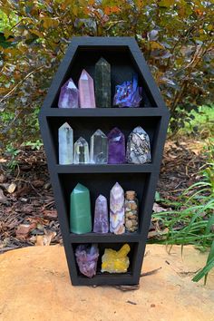 a black shelf filled with lots of different colored rocks next to some bushes and trees