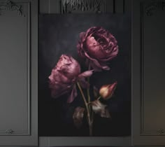 two pink flowers are in a vase on a table next to a wall with gray paneling