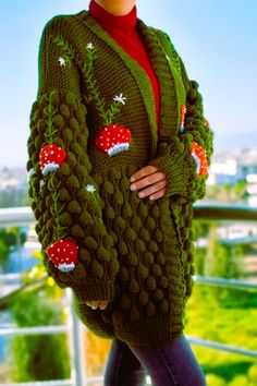 a woman wearing a green knitted cardigan with red mushrooms on the sleeves and sides