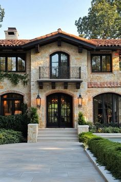 a large stone house with lots of windows and plants on the front porch, along with steps leading up to it