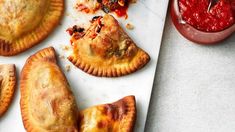 several pastries on a cutting board next to a small bowl of ketchup