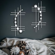 two metal wall art pieces on a bed with white sheets and pineconis in the foreground