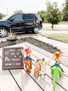 some toys are sitting on a wooden table in front of a black suv and sign