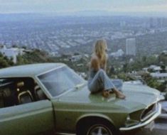 a woman sitting on top of a green car in front of a cityscape