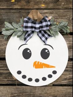 a snowman ornament is hanging on a wooden surface with leaves and plaid bow