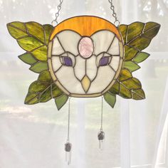 a stained glass owl hanging from a window with chain attached to it's face