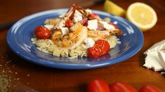 a blue plate topped with rice covered in shrimp and cherry tomatoes next to lemon wedges