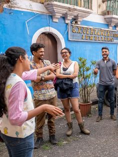 group of people standing in front of a blue and white building talking to each other