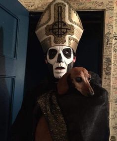 a man with a dog in front of him wearing a skull headdress and a cross on his forehead