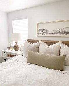 a bed with white linens and pillows in a bedroom next to a painting on the wall