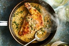 a pan filled with chicken and gravy on top of a table next to wine glasses