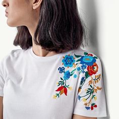 a woman wearing a white t - shirt with colorful flowers on the chest and shoulder