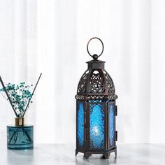 a blue lantern sitting on top of a table next to a vase filled with flowers