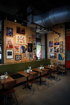 an empty restaurant with wooden tables and green bench seats, artwork on the wall behind them