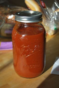 a mason jar filled with red liquid sitting on top of a wooden table next to bread