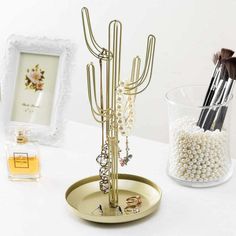 a gold jewelry holder with pearls and other accessories on a white table next to a framed picture