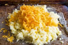 mashed potatoes and shredded cheese on a baking sheet with a fork next to it