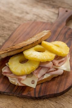 a ham and pineapple sandwich on a wooden cutting board with some slices of pineapple