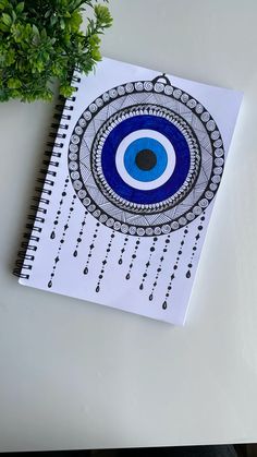 a spiral notebook with an eye drawn on it next to a potted green plant