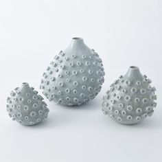 three white vases sitting next to each other on top of a table with holes in them