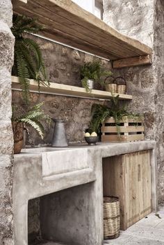 an outdoor kitchen with stone walls and shelves, potted plants on the counter top