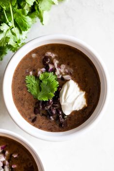 two bowls of black bean soup with sour cream and garnished cilantro