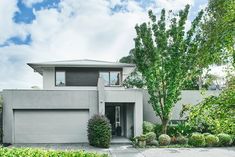 a modern house with trees and bushes in front of the house, on a sunny day