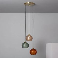 three different colored glass pendant lights hanging from a ceiling fixture in a room with white walls