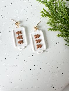 two white earrings with brown hearts hanging from them on top of a table next to a plant