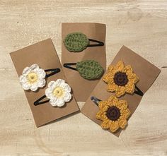 four small crocheted flower clips in brown paper on a wooden table with white and yellow flowers