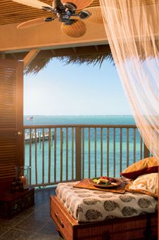 a bed sitting under a ceiling fan in a bedroom next to a balcony with an ocean view