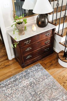 an ornate rug is on the floor next to a wooden dresser with a lamp and mirror