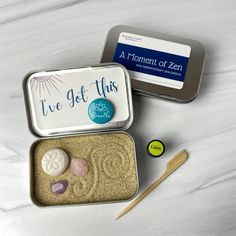 two tins filled with rocks and sand next to a pair of wooden knitting needles