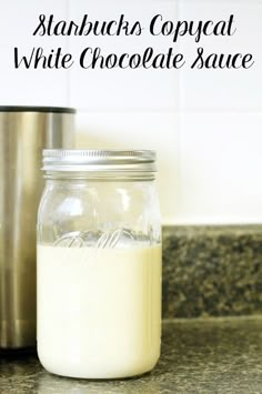 a glass jar filled with white chocolate sauce sitting on top of a counter next to a stainless steel shaker