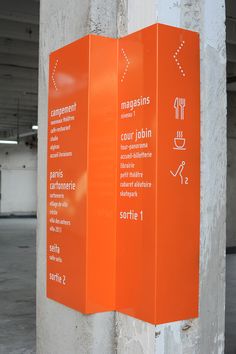 three orange signs on the side of a building in an underground parking garage area, with instructions for different things to do