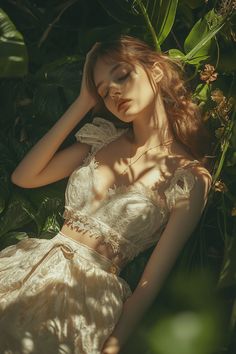 a woman in a white dress laying on the ground next to green plants and flowers