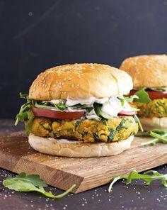 two sandwiches with vegetables and cheese are on a cutting board next to some greens in the background