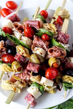 a white plate topped with meat and veggies on skewers next to tomatoes