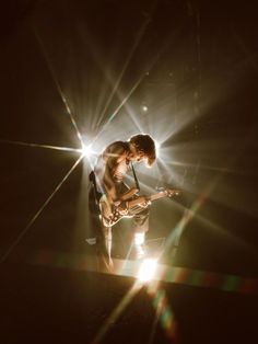 a man standing on stage with his guitar in front of the light from behind him