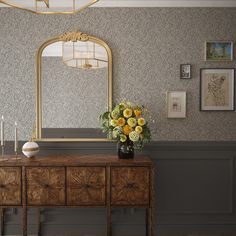 a vase with yellow flowers sitting on top of a wooden dresser next to a mirror