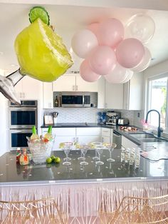 balloons are hanging from the ceiling above a kitchen counter with champagne glasses and fruit on it