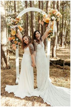 two women standing next to each other in front of an arch with flowers on it