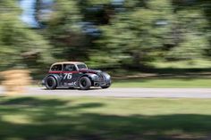 an old car driving down the road with trees in the background