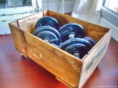 a wooden box filled with dumbs sitting on top of a hard wood floor next to a window